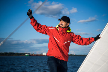 Young man skipper in red windbreaker and black cap sets the sails on a sailing yacht © romankosolapov
