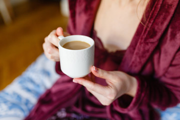 Morning coffee. Woman holding white Cup with black coffee sitting on bed in hotel. Young girl enjoys hot invigorating coffee in the morning