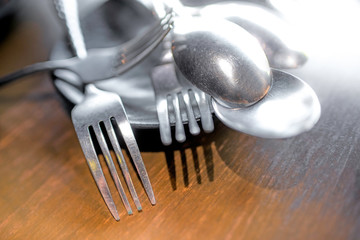 Spoon and fork placed in a black plate on a wooden table The windows are shining in the house.soft focus.