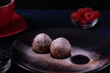 Homemade chocolate cake balls truffels sprinkled with powder sugar on black plate and red and black  raspberry with coffe cup   with dark background in rustic style.