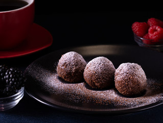Homemade chocolate cake balls truffels sprinkled with powder sugar on black plate and red and black  raspberry with coffe cup   with dark background in rustic style.