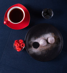 Homemade chocolate cake balls truffels sprinkled with powder sugar on black plate and red and black  raspberry with coffe cup   with dark background in rustic style.top view. closeup.