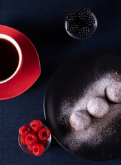 Homemade chocolate cake balls truffels sprinkled with powder sugar on black plate and red and black  raspberry with coffe cup   with dark background in rustic style.top view. closeup.