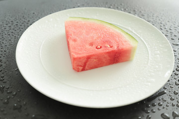 on a white ceramic plate are slices juicy, beautiful watermelon. A slice of watermelon lies on a black background with water droplets