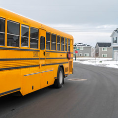 Fototapeta na wymiar Clear Square Side view of a school bus on a road passing through snowy homes in winter