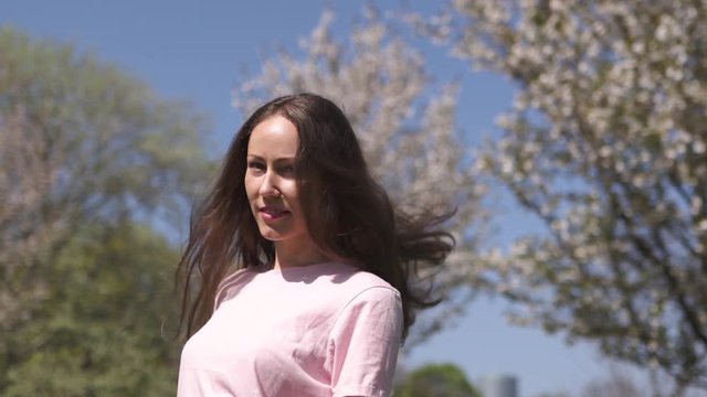 SLOW MOTION 120fps: Young happy traveler brown haired woman girl smiling and turning around in a new destination country with a pink sakura cherry blossom trees in Baltic states - Flying hair