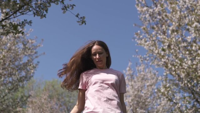 SLOW MOTION 120fps: Young happy traveler brown haired woman girl smiling and turning around in a new destination country with a pink sakura cherry blossom trees in Baltic states - Flying hair