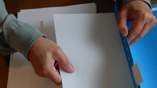 Hands are placing papers in a file folder .