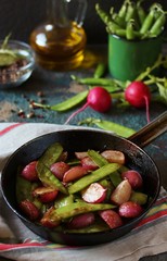 roasted young pods of peas and radish in a frying pan. light background. Soft focus