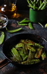 Fried young peas in a pan on a dark background.