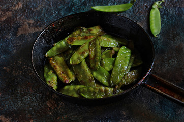Fried young peas in a pan on a dark background.