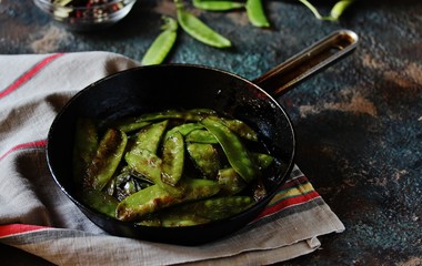 Fried young peas in a pan on a dark background.