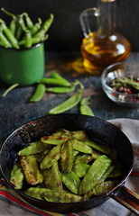 Fried young peas in a pan on a dark background.