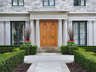 elegant double wooden front door of large suburban house with stone columns and  hedge