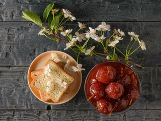 A bowl of Apple jam, bread, and a branch of flowers on a dark table. The view from the top. Flat lay.