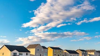 Fototapeta premium Clear Panorama Row of houses under a vibrant blue sky with fluffy clouds on a sunny day