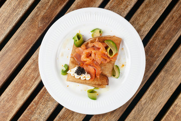 Top view of russian traditional blini with smoked salmon, black caviar, avocado and cream cheese for shrovetide