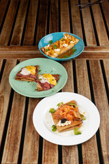 Crepes with pineapple and caramel sauce, smoked salmon and caviar, poached egg and bacon on a wooden rustic table
