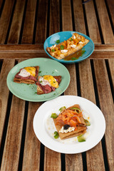Crepes with pineapple and caramel sauce, smoked salmon and caviar, poached egg and bacon on a wooden rustic table