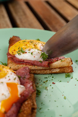 Cutting poached egg with knife on a pancake with ham and cheese