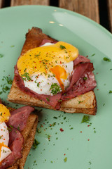 Crepes with poached egg, ham and cheese sauce on bright plate and rustic wooden table