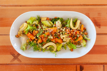 Bowl of vegetarian salad with greens, mini-corn, chickpea and quinoa on a light wooden table