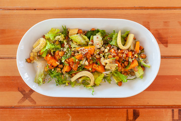 Bowl of vegetarian salad with greens, mini-corn, chickpea and quinoa on a light wooden table