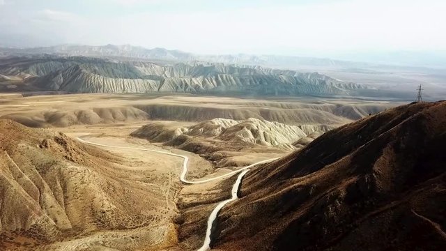 Incredible mountain road passing through a valley exiting the mountain pass. Insane golden mountains in Kyrgyzstan in the background view from the drone with car driving
