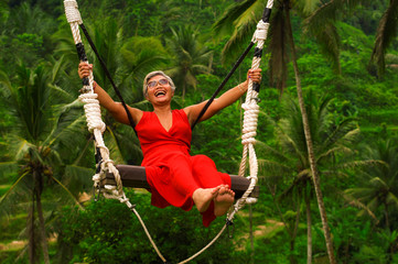 attractive happy middle aged 40s or 50s Asian Indonesian woman with grey hair riding rainforest...