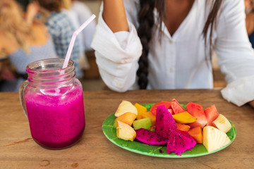 Healthy lifestyle concept. Beautiful smiling vegetarian woman drinking fresh smoothie juice with dragon fruit and eats fresh tropical fruits, Diet Concept.