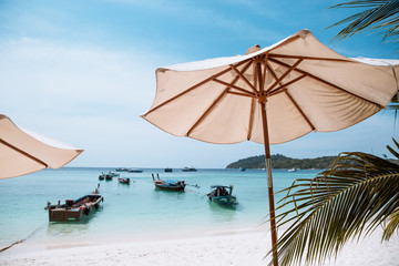 White umbrella on the tropical beach at daytime with long tail taxi boat. People