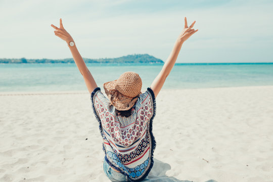 Back side view of the happy young woman in straw hat siting and relaxing on the beach.