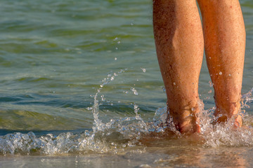 Legs of Bathers on the Seaside on Blur Blue Ocean Water Background.