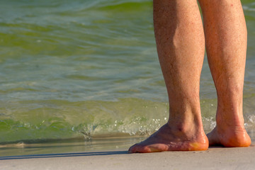 Legs of Bathers on the Seaside on Blur Blue Ocean Water Background.