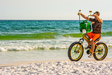Fototapeta premium Man Riding a Bycicle on White Sand on Blur Ocean Water Background. Destin Beach, Florida