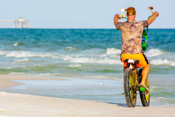 Man Riding a Bycicle on White Sand on Blur Ocean Water Background. Destin Beach, Florida
