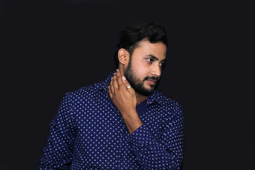 Fototapeta premium portrait of a young man model touching his neck with his hand in black background