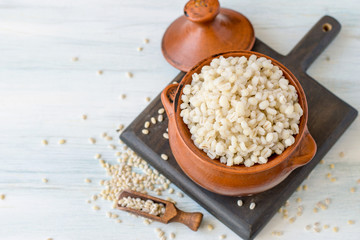 Barley porridge in a small earthen pot on a light wooden table. Selective focus.