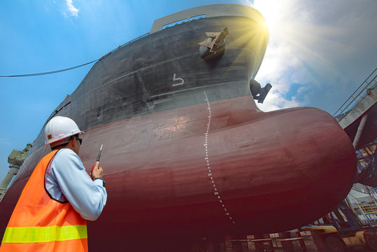Stevedore, port controller, Port Master, surveyor inspect the bulk head of commercial cargo ship in floating dry dock yard, recondition of overhaul repairing and repainting, working in dry dock yard