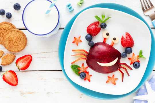Fun Food for kids. Cute smiling crab made of fresh fruits - apple, strawberry, blueberries and fresh mint - for a healthy breakfast with milk and biscuits