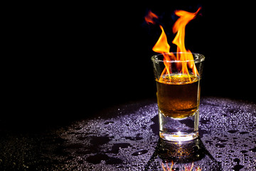 Hot alcoholic cocktail burning in shot glass  on black background.