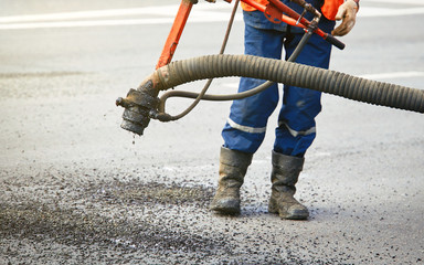 Professional worker in uniform during fast repair road surface. Operator of spray incjection...
