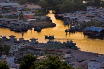 Obraz premium Lifestyle of people in the riverside village during the sunset, The ship is sailing on the river and golden light of the sky at sunset reflected on the water surface. Ban Pak Nam, Chumphon, Thailand.