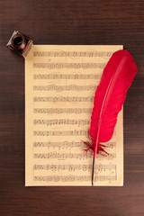 A piece of sheet music, shot from the top on a dark rustic wooden background with a quill pen and an ink well