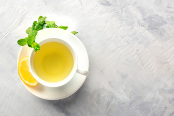 Obraz na płótnie Canvas A cup of green tea with lemon and mint, shot from the top on an abstract grey background with a place for text