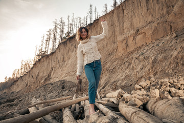  portrait of young trendy woman dressed in brown knit sweater made of natural wool and jeans laughing, smiling, posing n the beach; in the background  sandy slope with trees.