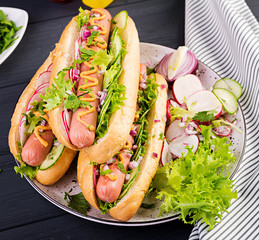 Hot dog with  sausage, cucumber, radish and lettuce on dark wooden background. Summer hotdog.