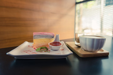Colorful crepe cake in white plate with strawberry sauce and hot coffee