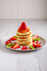 Stack of hot flapjacks served with fresh strawberries and kiwi on white wooden table