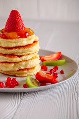 Stack of hot flapjacks served with fresh strawberries and kiwi on white wooden table